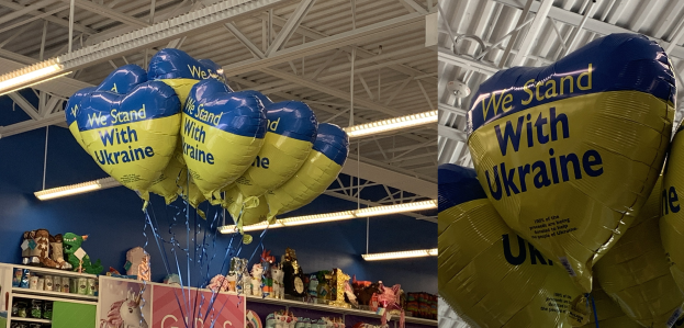 Ein Geschäft mit bunten Luftballons an der Decke, Spielzeug und Artikeln auf Regalen und heller Beleuchtung, die eine festliche Atmosphäre schafft.