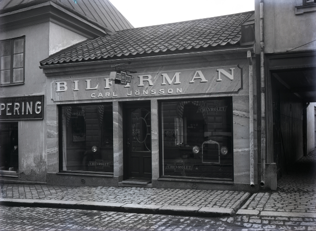 Ein Schwarz-Weiß-Foto eines Gebäudes mit einer 'Bilferman'-Aufschrift, Fenstern, einer Tür und Schildern mit Text, mit einer Straße unten.