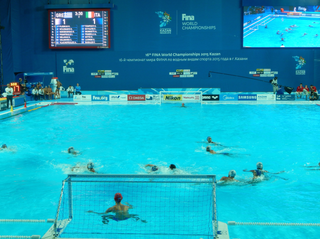 Gruppe von Athleten beim Wasserballspielen in einem Pool während der 2016 FINA-Weltmeisterschaften in Kazan, mit einem Netz, das den Pool teilt, und Zuschauern auf der linken Seite.