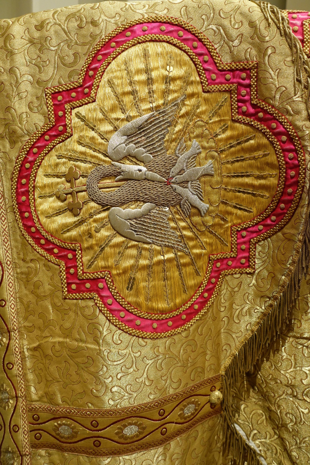 Nahaufnahme eines Priestergewänders mit aufwendiger goldener und roter Stickerei mit einem luxuriösen, herrschaftlichen Design gegen einen neutralen Wandhintergrund.