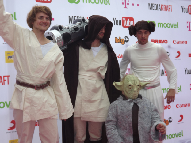 Eine Gruppe von Menschen in Star-Wars-Kostümen, die auf einem roten Teppich posen und im Hintergrund ein Banner zu sehen ist.
