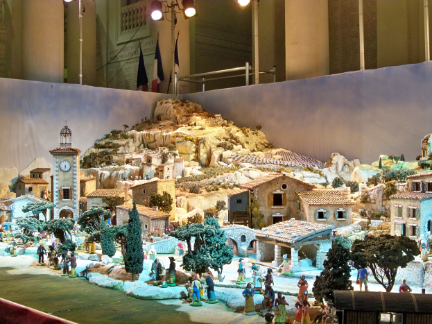 Ausstellung im Museum: Detailgetreue Darstellung einer Krippe mit Figuren, Strukturen und Beleuchtungselementen vor Häuser, Bäume und einen Kirchturm.