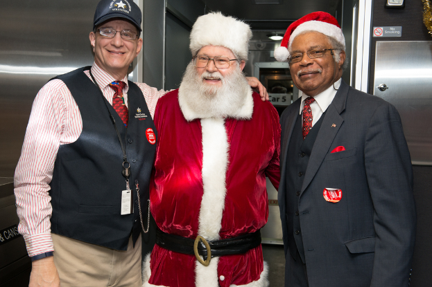 Eine Gruppe von Menschen mit Brillen, Mützen, Krawatten, ID-Karten und Ausweisen, mit einer Person in einem Weihnachtsoutfit, die vor einer Stahlwand mit Lichtern, Schildern und anderen Gegenständen im Hintergrund steht.