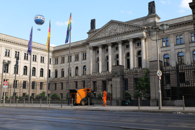 Großes modernes Gebäude mit vielen Fenstern, als Bundestag in Berlin, Deutschland identifiziert, umgeben von Straßeninfrastruktur, Passanten, Fahrzeugen und Bäumen unter einem bewölktem Himmel.