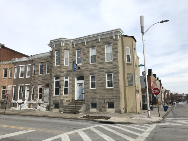 Eine Reihe moderner Häuser an einer Straßenecke in Philadelphia, mit Fahrzeugen, Bäumen und einem bewölkten Himmel im Hintergrund.