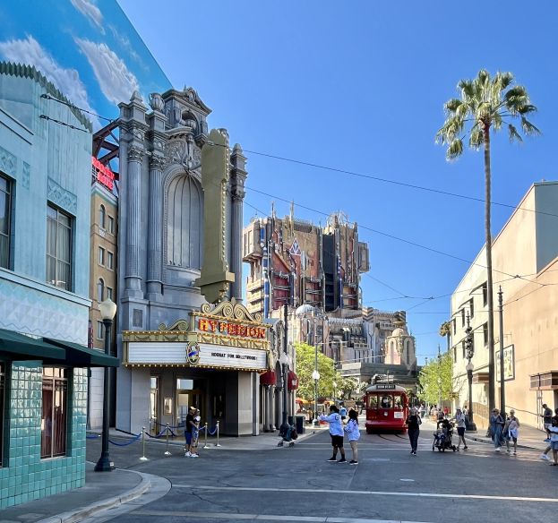 Lebendige StraßenSzene auf dem Universal Studios Hollywood mit Passanten, einem Fahrzeug, Bäumen, Pfosten und Gebäudefassaden unter einem sichtbaren Himmel.