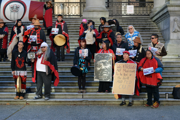 Eine Gruppe von Menschen auf einer Treppe, die Plakate und einen Lautsprecher halten, mit einem Banner im Hintergrund.