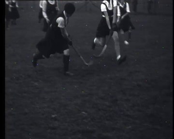 Schwarzes und weißes Foto von jungen Mädchen, die auf einem Outdoor-Feld Feldhockey spielen, jede hält einen Hockey-Schläger in der Hand.