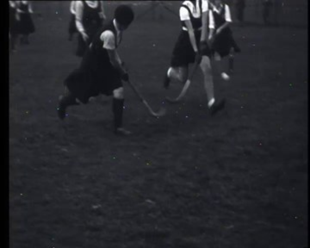 Schwarzes und weißes Foto von jungen Mädchen, die auf einem Outdoor-Feld Feldhockey spielen, jede hält einen Hockey-Schläger in der Hand.