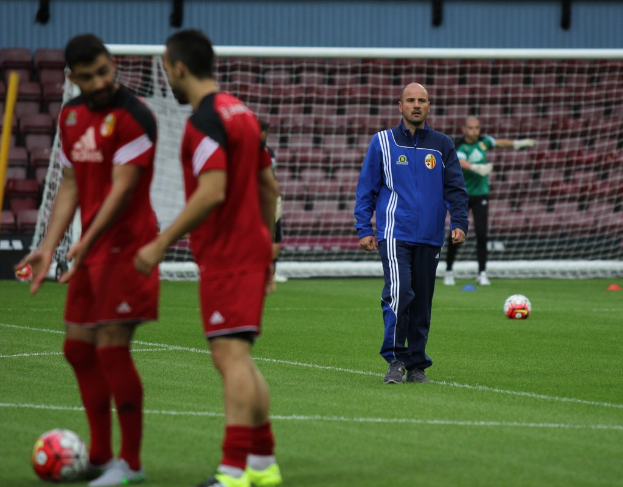 Ein Fussballfeld mit darauf stehenden Spielern, zwei Bällen und einer leeren Tribüne im Hintergrund.