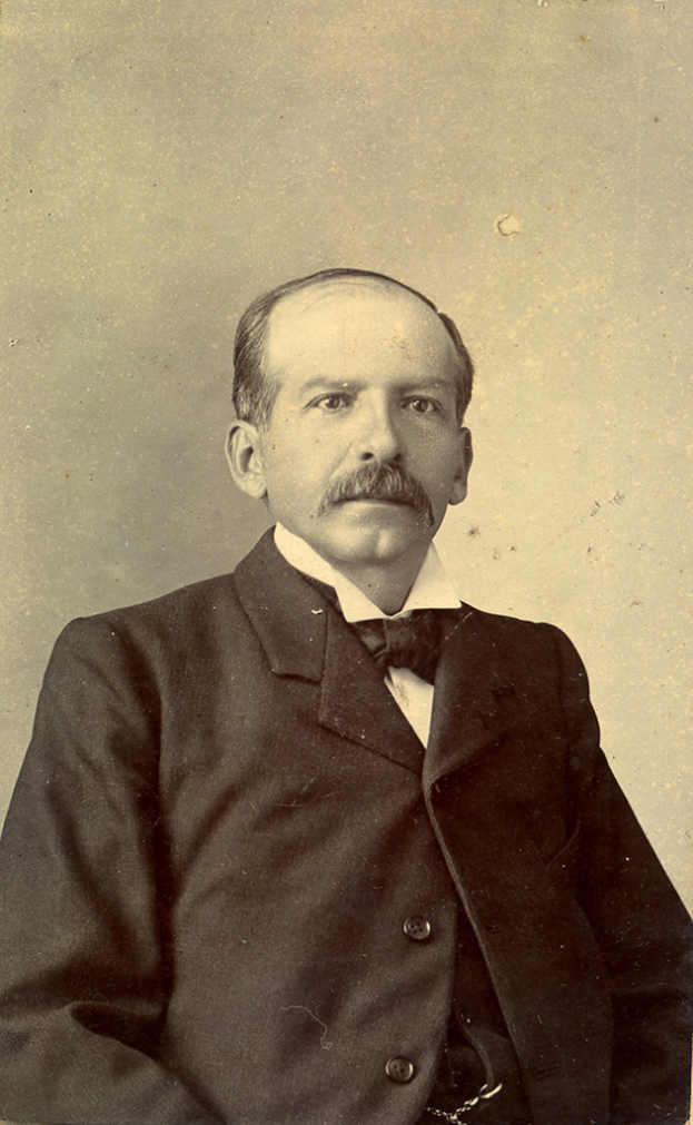 Ein älterer Mann in einem Anzug vor einer Wand.