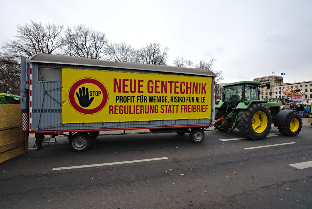 Ein Lastwagen mit einer Aufschrift auf der Rückseite fährt auf einer Straße in Deutschland, umgeben von Menschen, Bäumen, Gebäuden und einem klaren blauen Himmel, wahrscheinlich Teil einer Demonstration.