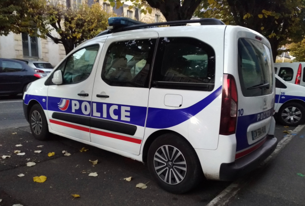 Ein Polizeiwagen parkt auf einer Straße, die von Gebäuden, Bäumen und abgefallenen Blättern gesäumt ist.
