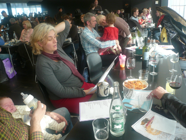 Einblicke in ein volles Restaurant mit Gästen an Tischen, die mit Gläsern, Tellern mit Essen, Getränkeflaschen, Speisekarten und anderen Gegenständen ausgestattet sind.