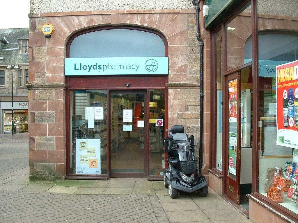 Apothekenladen mit einem vor dem Gebäude geparkten Auto und einem Gebäude in der linken Ecke.