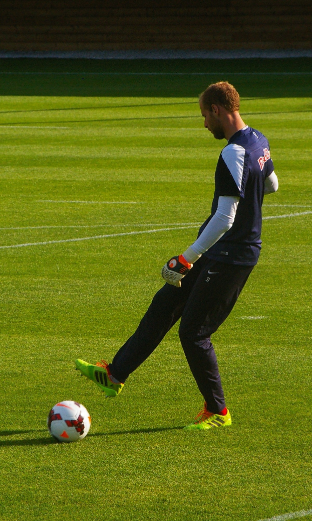 Ein Mann in einem Fußballtrikot schießt einen Fußball auf einem Fußballfeld und sieht entschlossen aus.