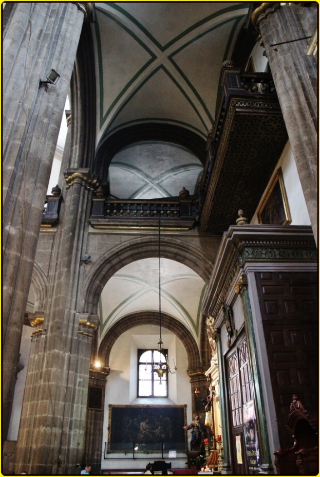 Ein prunkvoller Innenraum eines Palasts mit Schränken, beleuchteten Säulen, Wandskulpturen, einem großen Rahmenbild und einer Deckenleuchte.