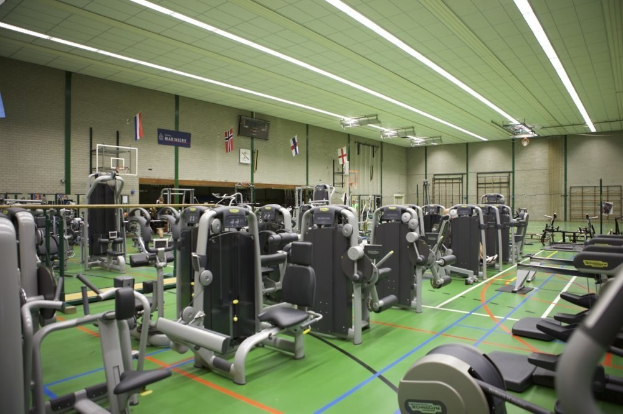Ein geräumiges Fitnessstudio mit verschiedenen Trainingsgeräten, einer Wand mit Flaggen und Deckenbeleuchtung.