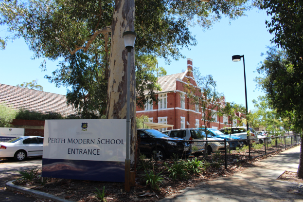 Eintritt zum Perth Modern School mit einem Schild, Bäumen, Pflanzen, einem Zaun, einem Straßenpfahl, geparkten Autos, Gebäuden mit Fenstern und einem bewölkten Himmel.