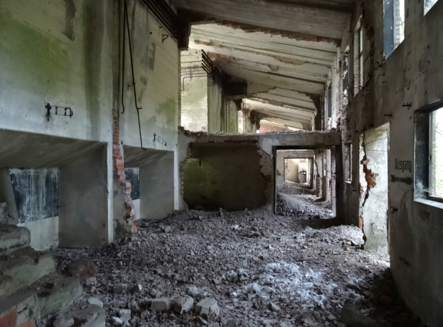 Altes Gebäude mit erheblichen strukturellen Schäden, zerbrochene Fenster, verstreute Trümmer, freiliegende Rohre und Schutt, die Verfall anzeigen.