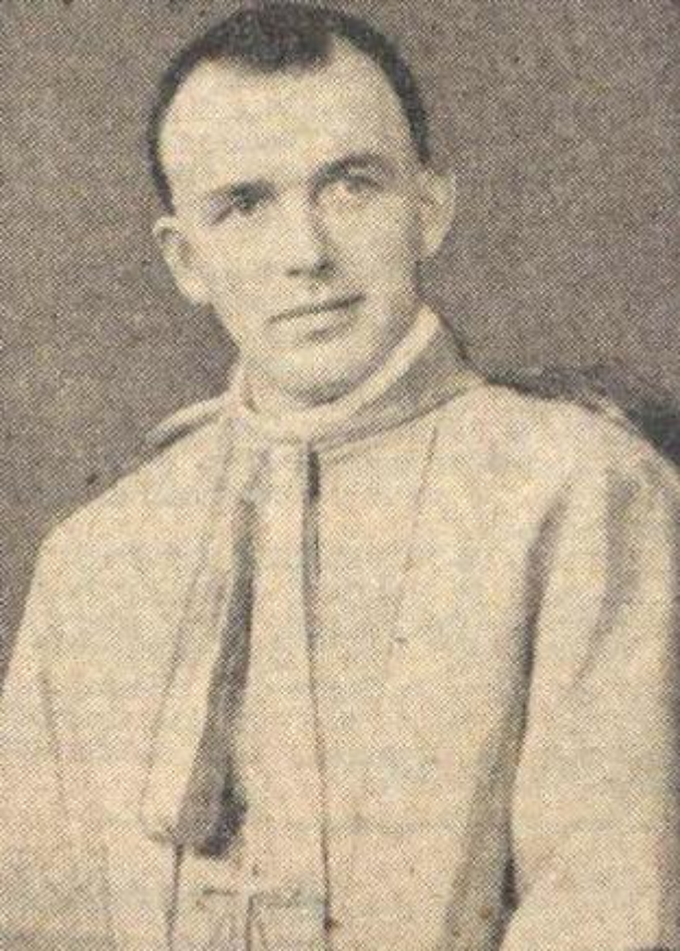 Ein Schwarz-Weiß-Foto eines Mannes in Priesterkleidung, der eine weiße Robe mit schwarzem Kragen und Manschetten und einen schwarzen Hut mit einer weißen Feder trägt, mit gefalteten Händen und einem ernsten Gesichtsausdruck.