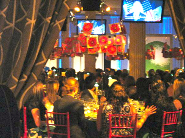 Eine Gruppe von Menschen an Tischen mit Essen, Fernsehern, Lampen, hängenden Papieren und Vorhängen in einer Party-ähnlichen Umgebung.