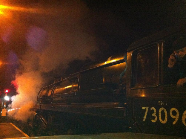 Eine Dampflokomotive auf Schienen unter einem dunklen Himmel.