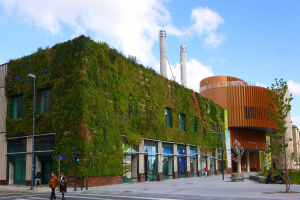 Ein großes Gebäude mit einer grünen Wand an der Seite, umgeben von Straßeninfrastruktur, Fahrzeugen, Fußgängern, Bäumen und einem bewölkten Himmel, Teil des Green Building Project.