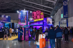 Eine große Gruppe von Menschen vor einem Stand auf einer Messe, einige halten Taschen und Schilder mit der Aufschrift "Indie Game Development Award 2019" im Hintergrund.
