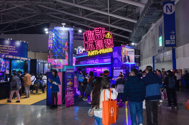 Eine große Gruppe von Menschen vor einem Stand auf einer Messe, einige halten Taschen und Schilder mit der Aufschrift "Indie Game Development Award 2019" im Hintergrund.