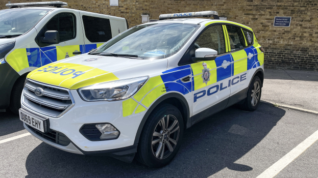 Zwei Polizeiwagen nebeneinander auf einem Parkplatz mit einer Wandtafel im Hintergrund geparkt.