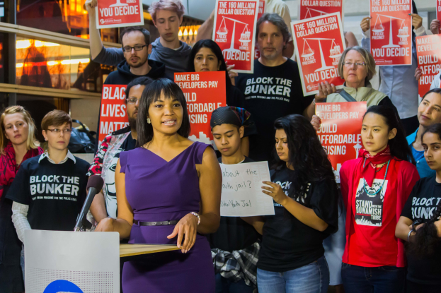 Eine Black Lives Matter-Aktivistin spricht vor einem Publikum mit Mikrofon, das Plakate hält, mit Lichtern und anderen Gegenständen im Hintergrund.