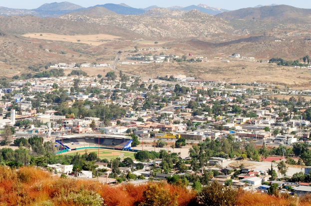 Eine Landschaft mit H├Ąusern, B├Ąumen, Strommasten, H├Ąngen und einem klaren Himmel.