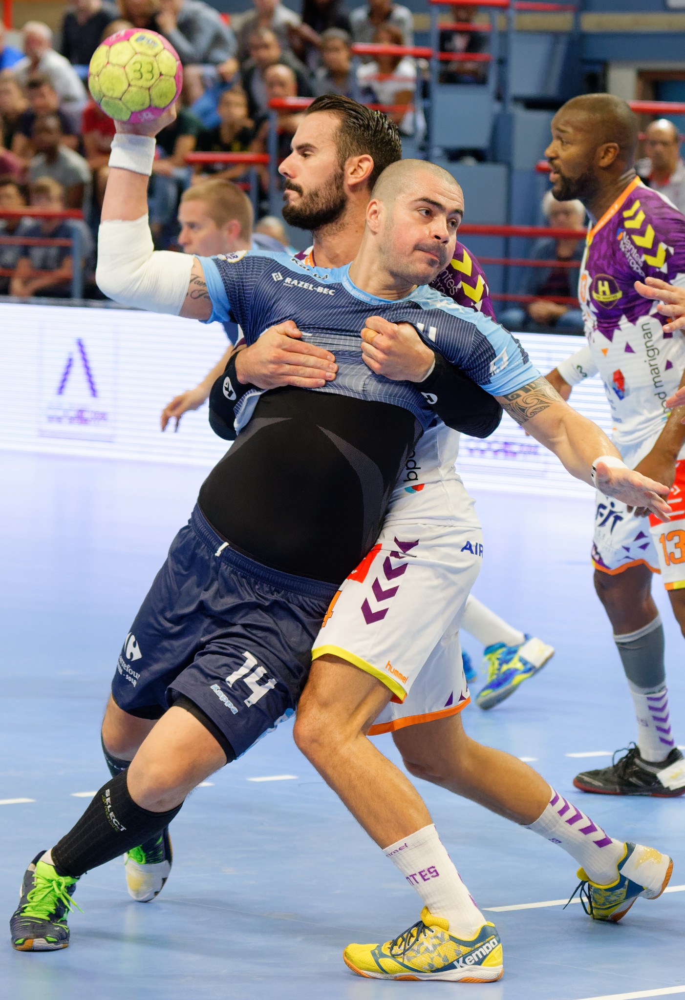 Eine Gruppe von Männern, die Handball in einem Stadion spielen, wobei einer den Ball hält.