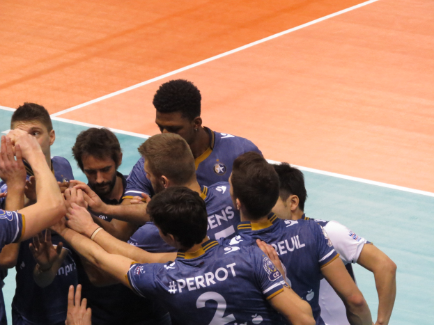 Gruppe von Männern in blauen "Ligue 1"-T-Shirts feiert auf einem Volleyballfeld.
