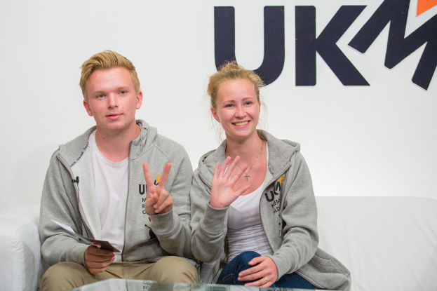 Ein Paar in passenden Jacken auf einem Sofa sitzend mit "UKM" im Hintergrund.