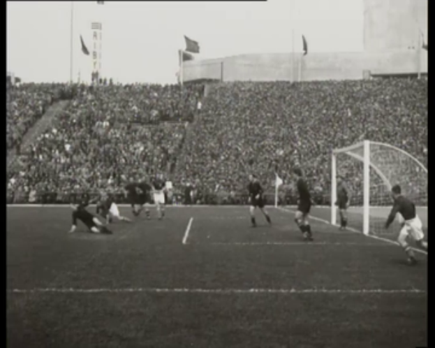 Ein Schwarz-Weiß-Foto eines Fussballspiels in einem Stadion, mit Spielern auf dem Feld und einem Torpfosten auf der rechten Seite, Zuschauern in den Rängen, Fahnen und einem klaren Himmel, mit Text oben und unten, der "1958-1958 WM-Finale - Manchester United v Liverpool" lautet.