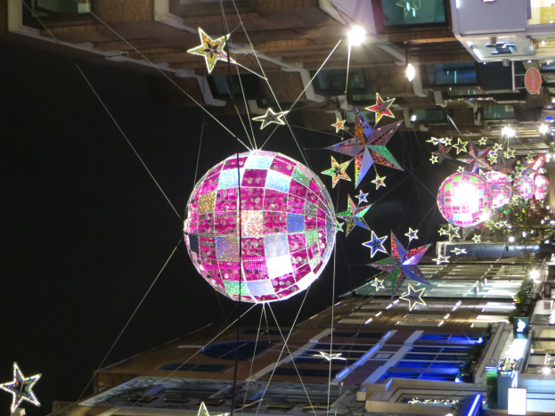 Eine stadtstra├če bei Nacht voller Lichter und Deko, mit einer gro├čen Diskokugel, die von einem Geb├Ąude h├Ąngt und eine festliche Atmosph├Ąre schafft.